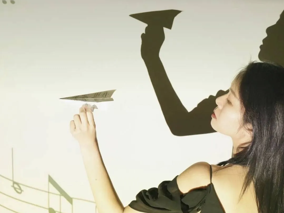 Yueheng Lin holding a paper airplane against projected musical notes